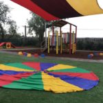 Outdoor play space with playground, shaded area, colourful parachute.